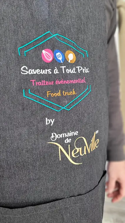 Tablier gris brodé aux logos « Saveurs à Tout Prix » et « Domaine de Neuville »