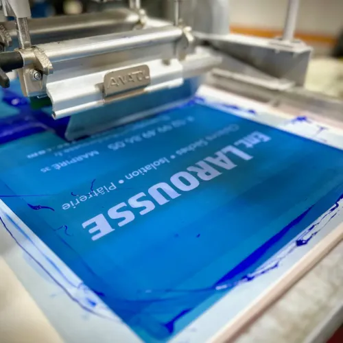 Écran de sérigraphie et racle : impression d’un texte blanc sur fond bleu à l’atelier HOP Textile