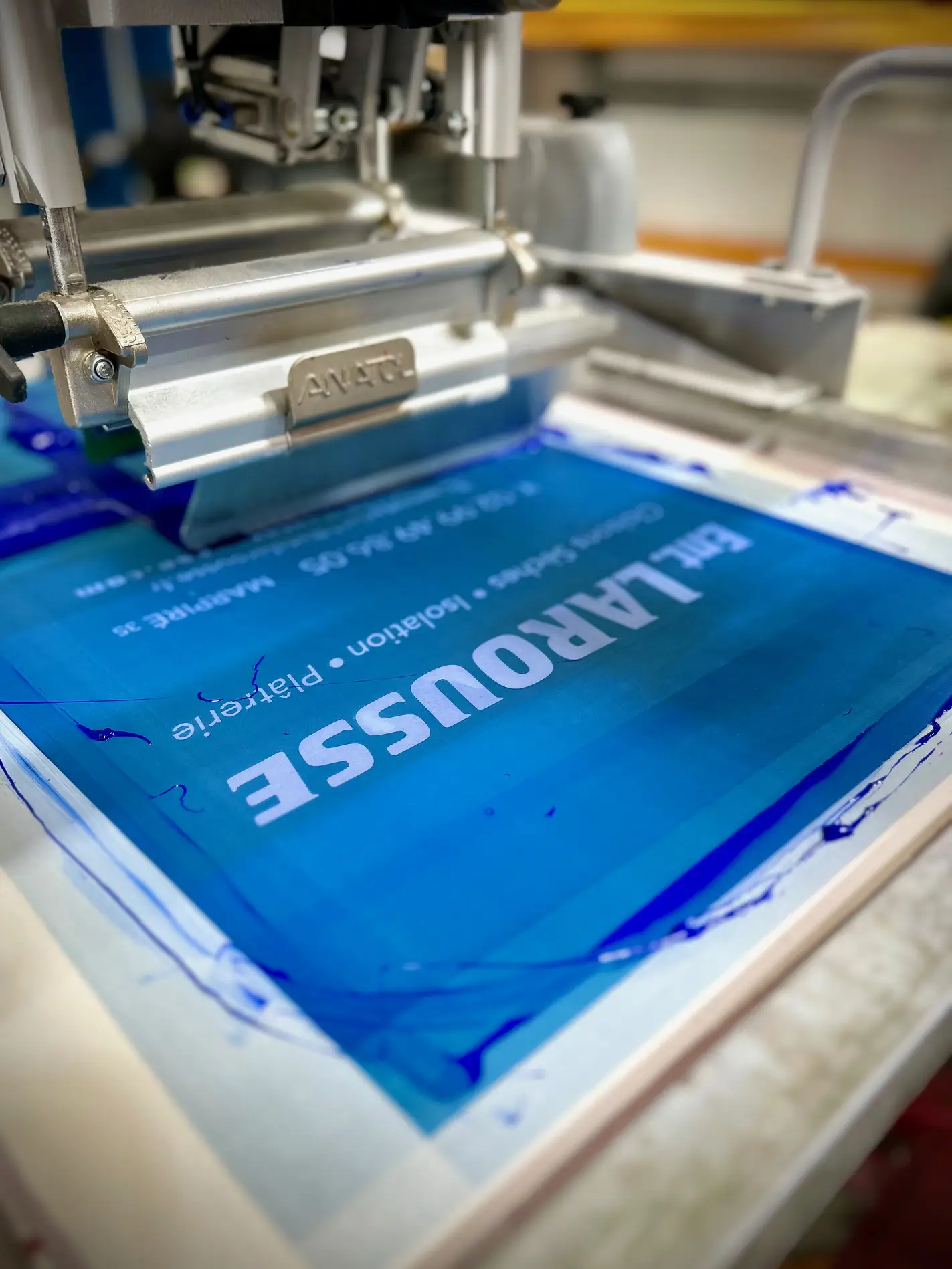 Écran de sérigraphie et racle : impression d’un texte blanc sur fond bleu à l’atelier HOP Textile