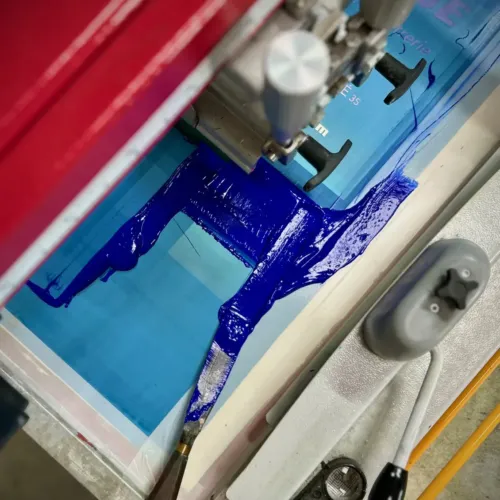Encre bleue étalée sur un écran de sérigraphie, sous la racle de la machine
